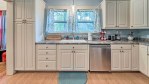 A kitchen with white cabinets, a stainless steel dishwasher, a window with curtains, and a countertop with various appliances. - Burgaw House w/ Large Covered Porch & Swing! (Burgaw)