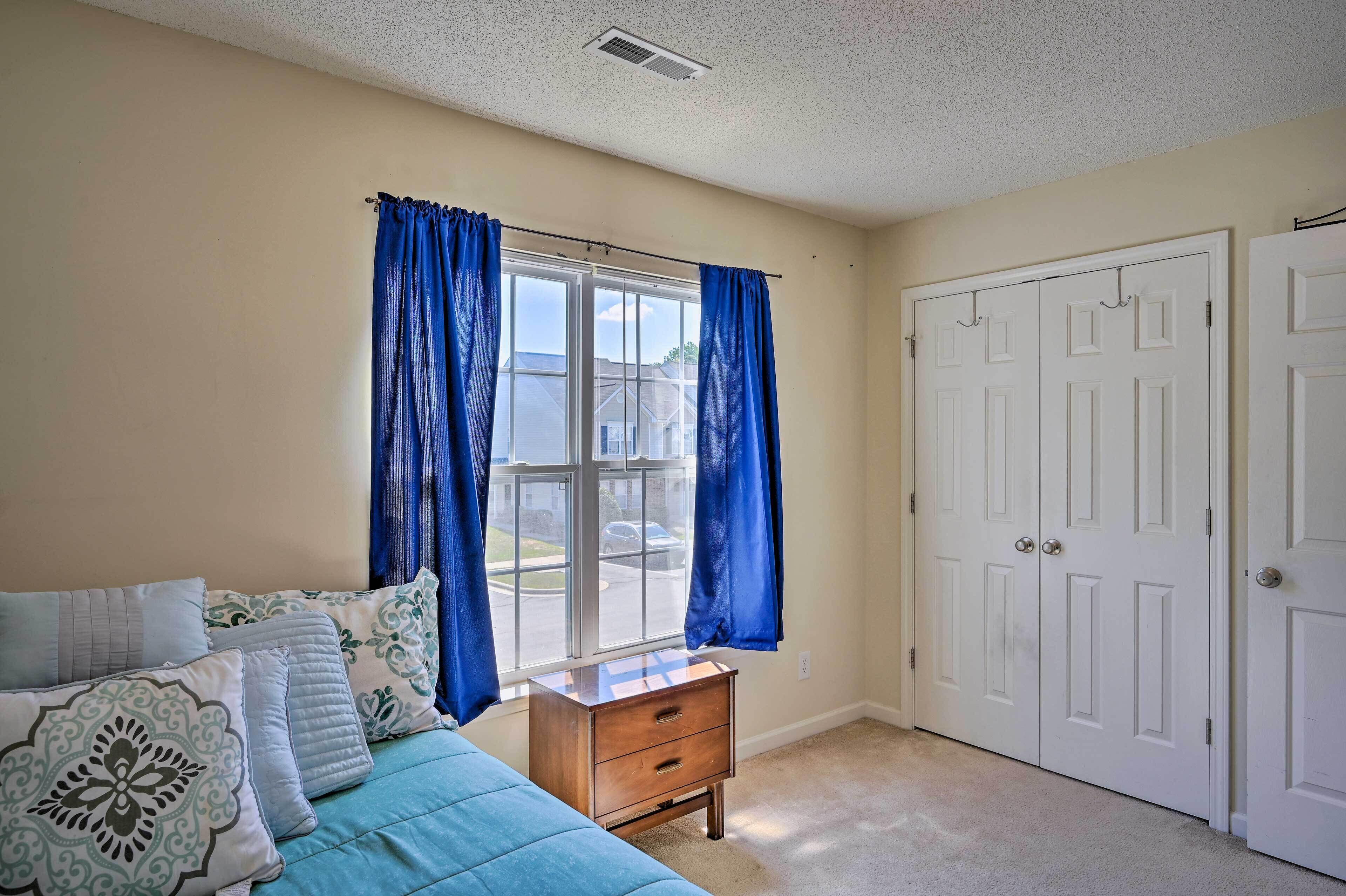 A bedroom with a bed, a nightstand, a window with curtains, and a set of white doors.