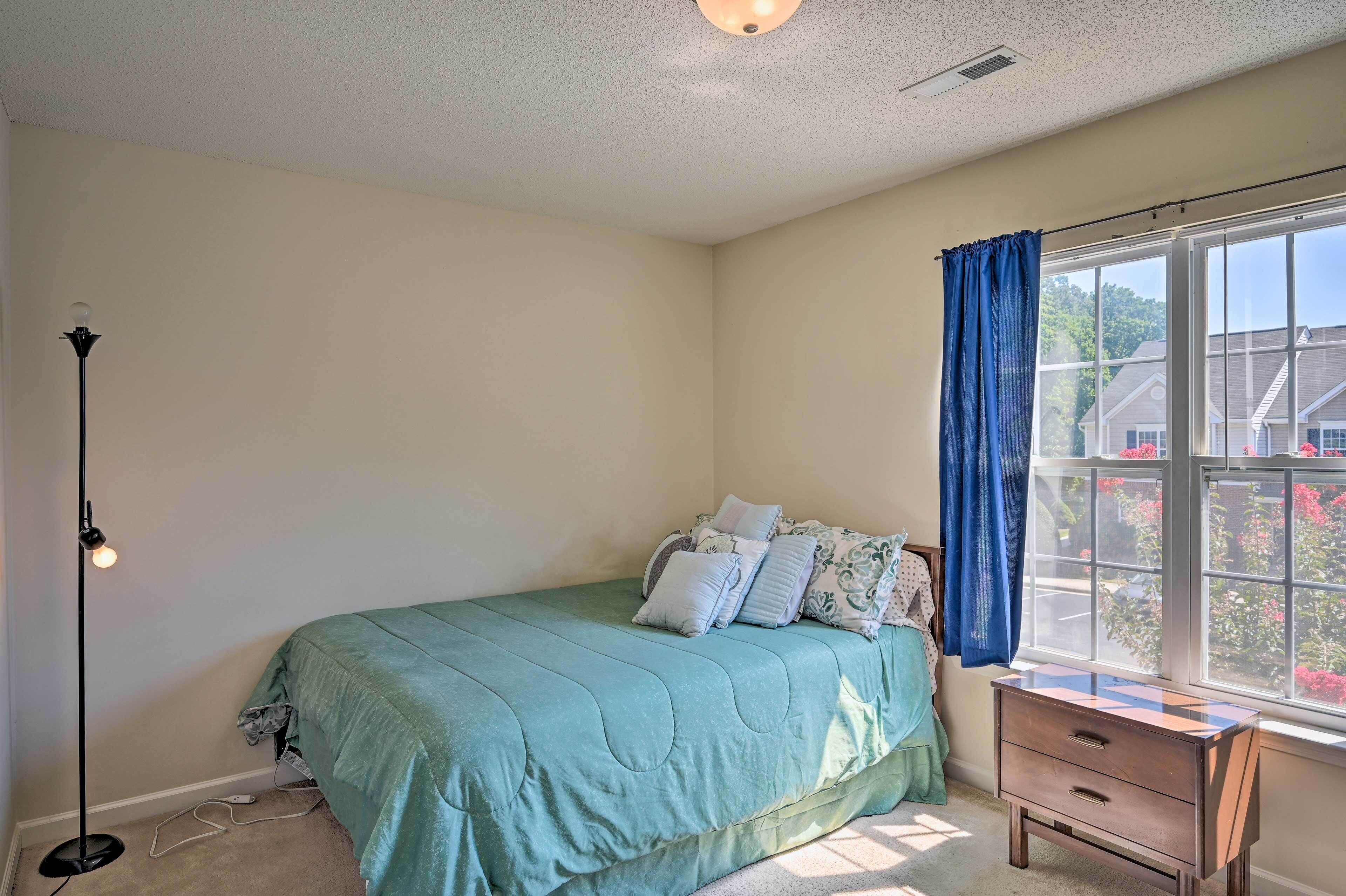 Un dormitorio con cama, mesita de noche, lámpara y ventana con cortinas.
