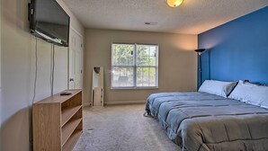A bedroom with a bed, a TV mounted on the wall, a window, and a ceiling light.