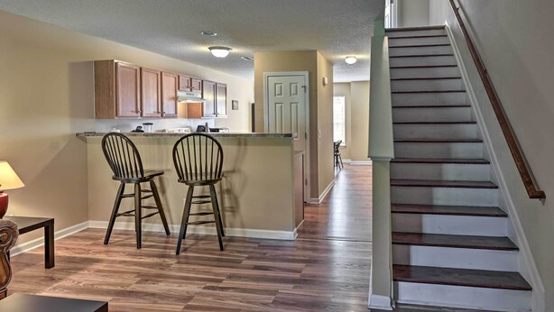 A kitchen with wooden cabinets, a central island with two chairs, and a staircase leading to another level.