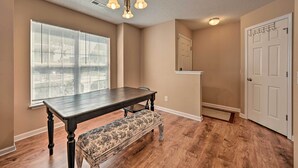 A dining area with a dark wooden table and bench, beige walls, and a large window with blinds.