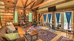 L’intérieur chaleureux d’un chalet avec des poutres en bois, une cheminée, une bibliothèque et un coin salon confortable.