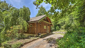 Un chalet rustique en bois, avec une allée en gravier, entouré d’une végétation luxuriante et d’arbres.