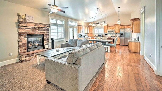 A spacious living room with a stone fireplace, a large gray sectional sofa, and a dining area with a wooden table. - Bellemont Family Home w/ Hot Tub & Playground Set (Flagstaff)