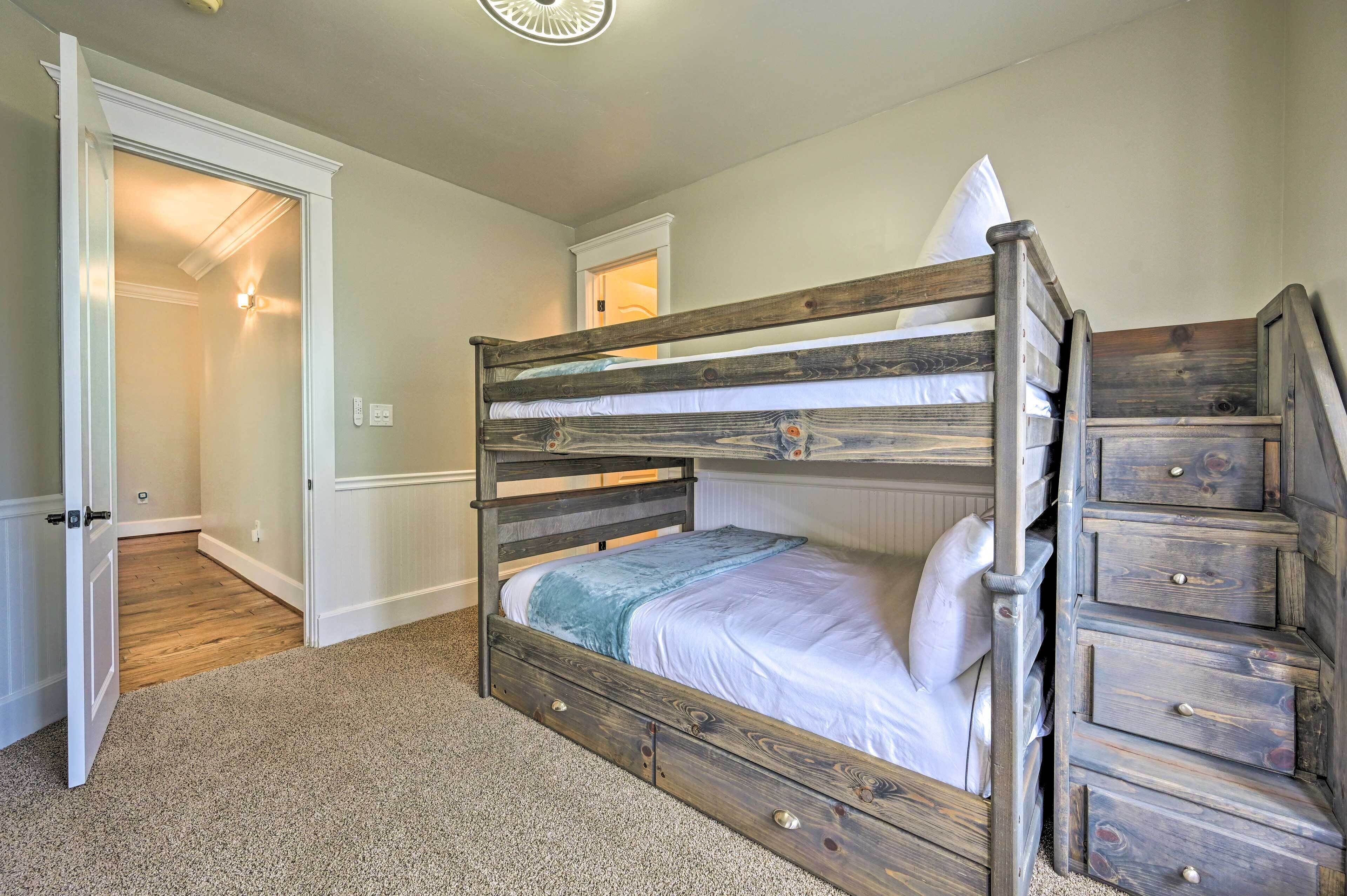 A bunk bed with a wooden frame and drawers, carpeted floor, and a door leading to another room.