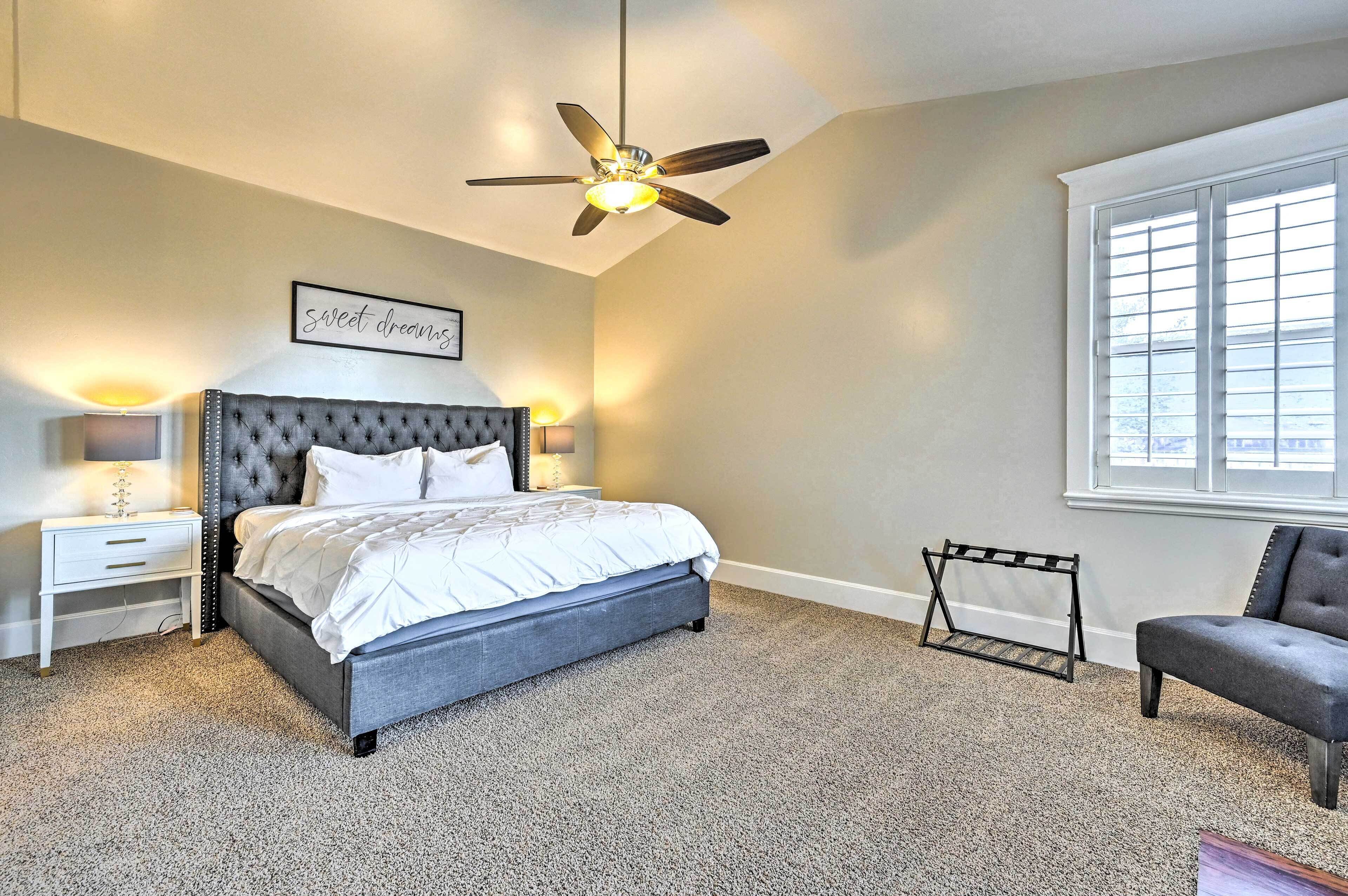 A bedroom with a bed, a ceiling fan, a bedside table, a chair, and a window.