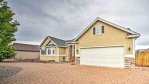 A two-story house with a garage, a covered porch, and a brick driveway. - Bellemont Family Home w/ Hot Tub & Playground Set (Flagstaff)