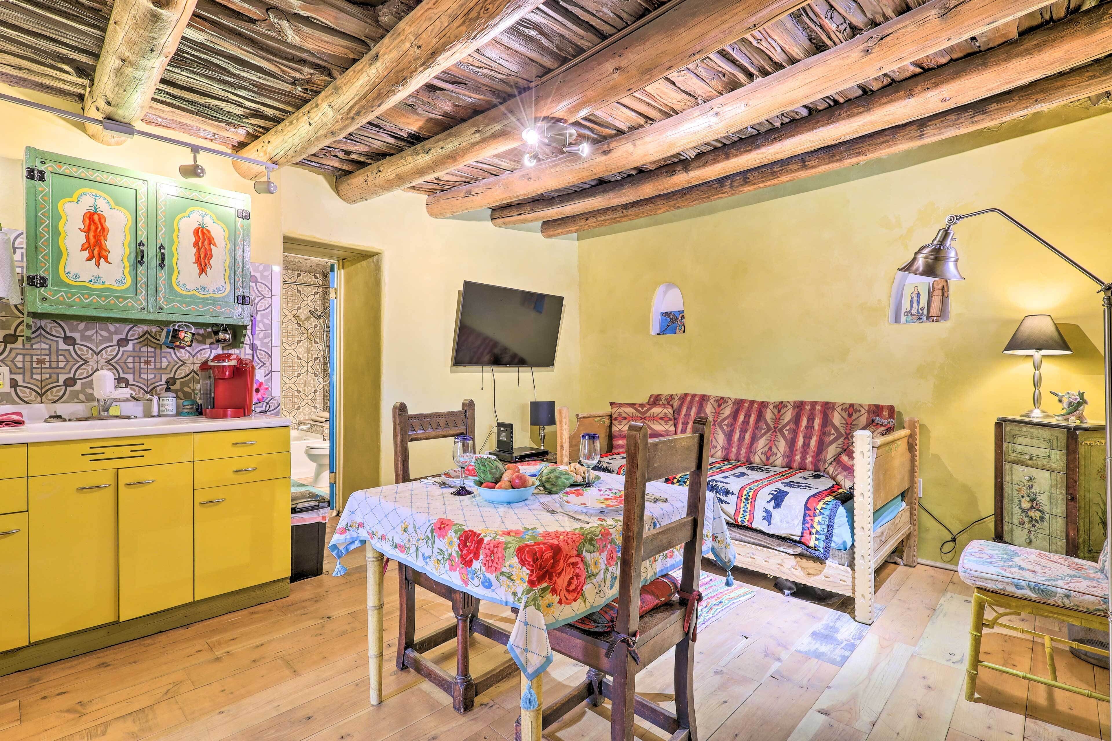 A rustic kitchen with wooden beams, a dining table with a floral tablecloth, and a wooden bench.