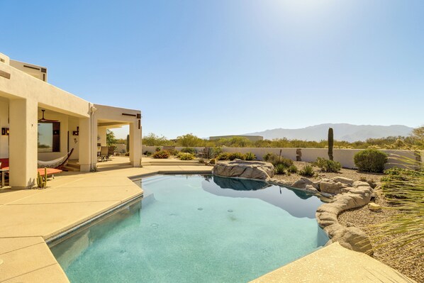 A pool with clear water, surrounded by rocks and plants, with a view of mountains in the background.