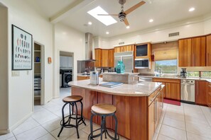 A modern kitchen with a central island, wooden cabinets, stainless steel appliances, and a ceiling fan. - Oro Valley Airpark Estate w/ Pool & Mtn Views (Oro Valley)