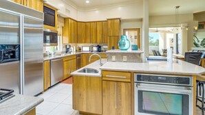 A modern kitchen with wooden cabinets, stainless steel appliances, a large island with a sink, and a ceiling fan. - Mtn-view Oasis w/ Pool, Spa & Gym in Oro Valley! (Oro Valley)