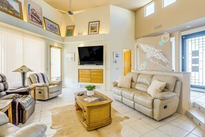 A living room with a flat-screen TV, leather sofas, a coffee table, and a large window.