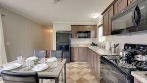 A modern kitchen with a dining area, featuring stainless steel appliances, wooden cabinets, and a checkered floor. - Cozy Cabin: Community Pool & Lakefront Beach! (Cassopolis)