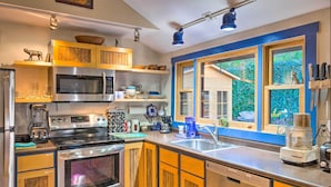 A modern kitchen with stainless steel appliances, wooden cabinets, and a large window offering a view of greenery. - Tranquil Abode w/ Garden, Sauna & Cold Plunge (Asheville)