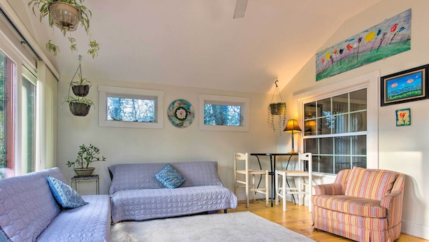A living room with two sofas, a patterned armchair, a dining table, and a large window. - Tranquil Abode w/ Garden, Sauna & Cold Plunge (Asheville)
