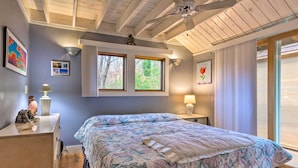 A bedroom with a large bed, two windows, a ceiling fan, and a view of trees outside. - Tranquil Abode w/ Garden, Sauna & Cold Plunge (Asheville)