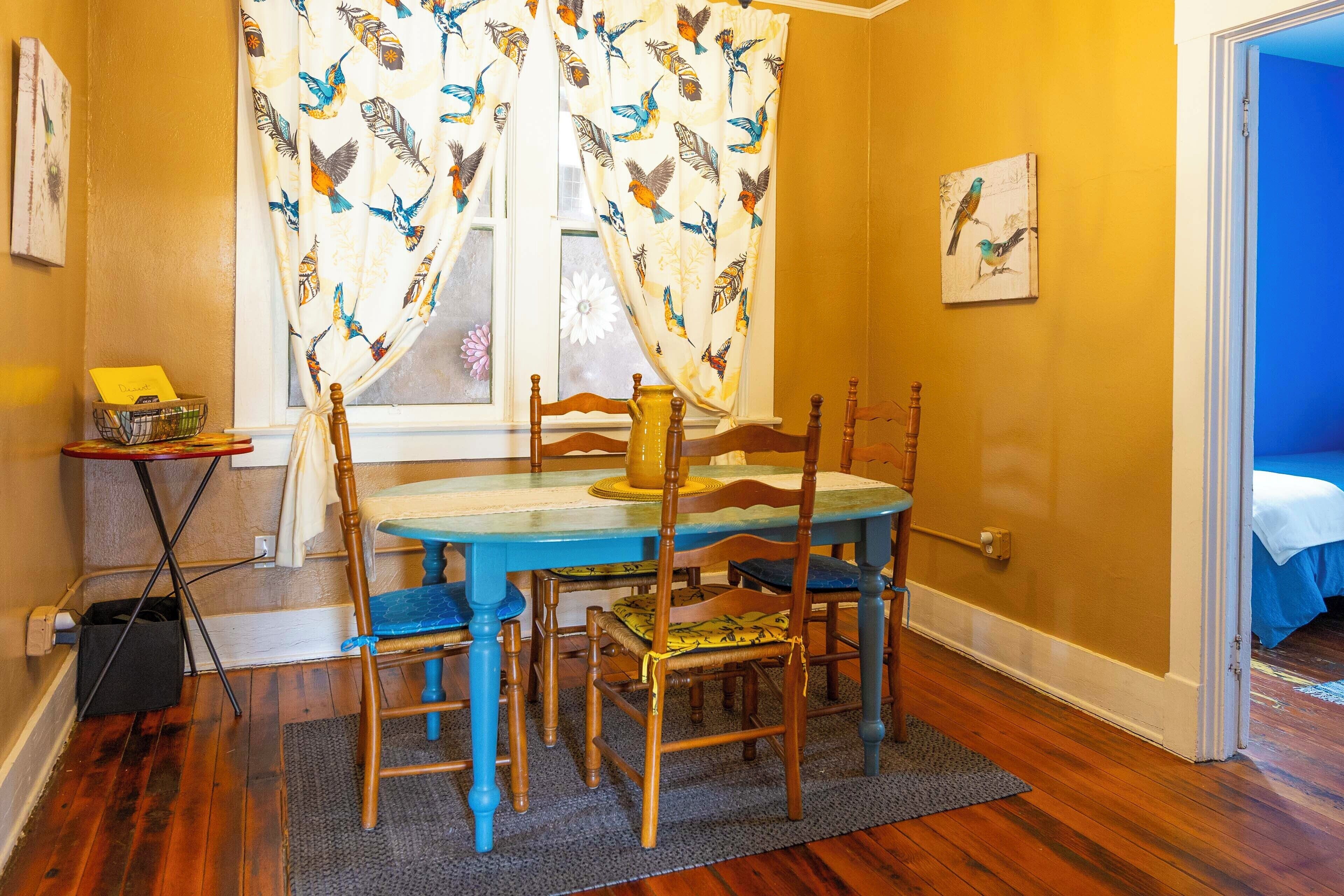 A dining area with a round table, four chairs, and a window with curtains.