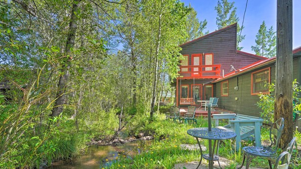 Een chalet met een rood dak en groene muren, gelegen in een natuurlijke omgeving met een beekje en groen.