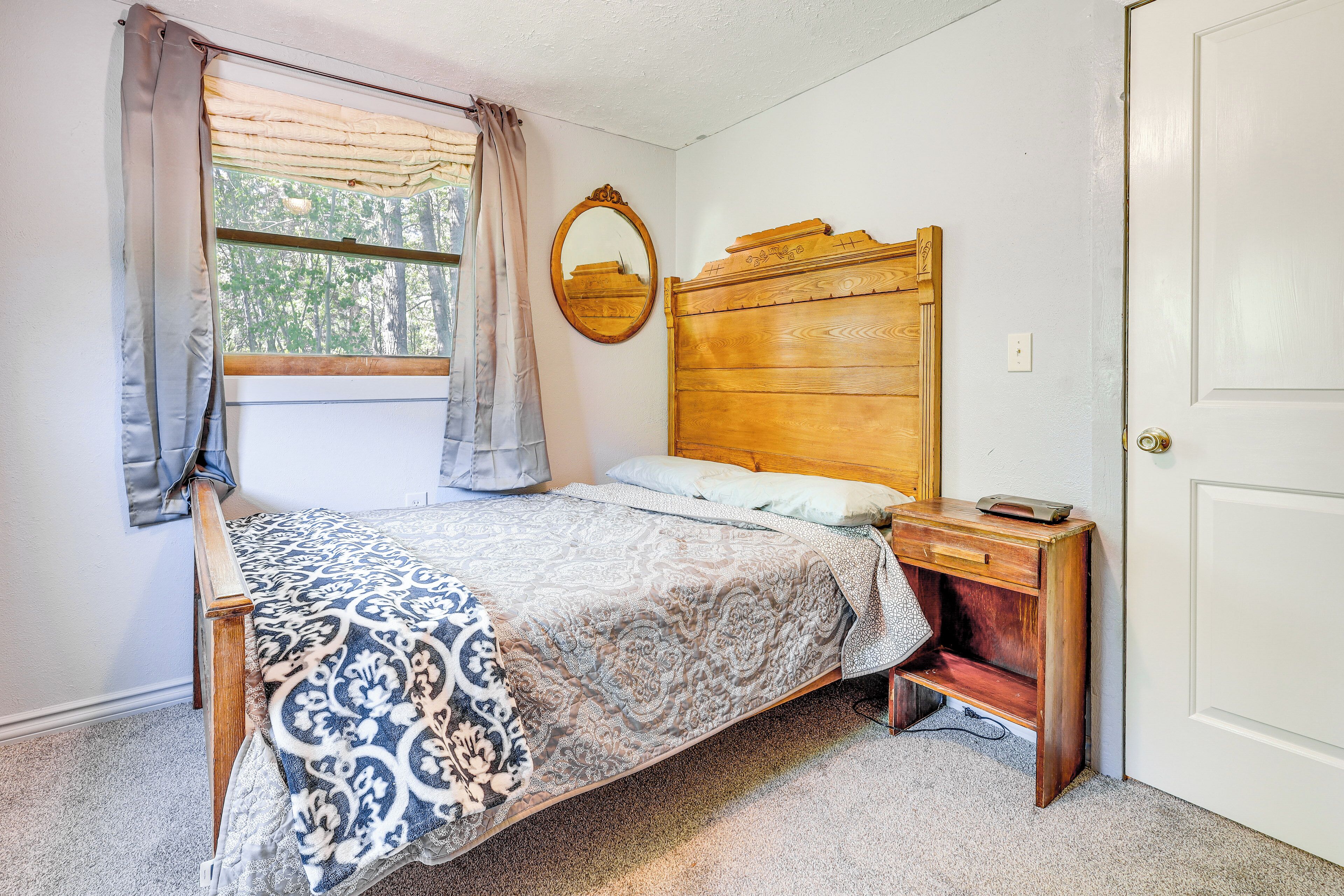 Quarto com cama de madeira, mesa de cabeceira, espelho e janela com cortinas.