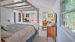 Een slaapkamer met een bed, bureau, stoel en groot raam.