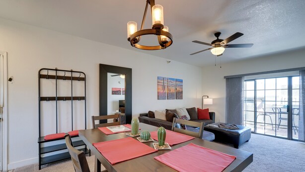 A modern living room with a dining area, a ceiling fan, a chandelier, and a large window with a view.