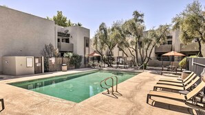 A swimming pool with lounge chairs and a fenced area, surrounded by trees and buildings.