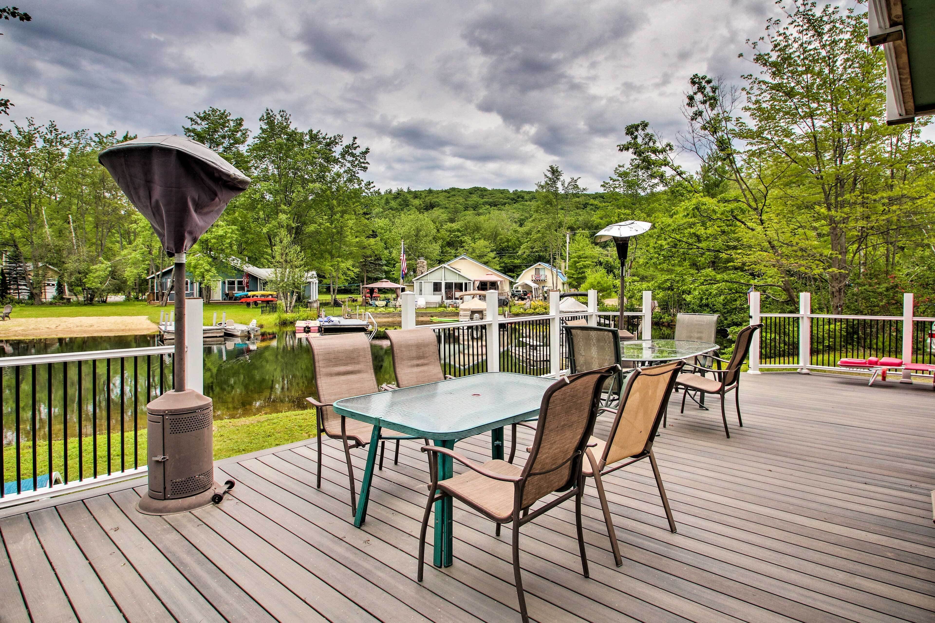 A wooden deck with a glass table and chairs, overlooking a pond and houses.