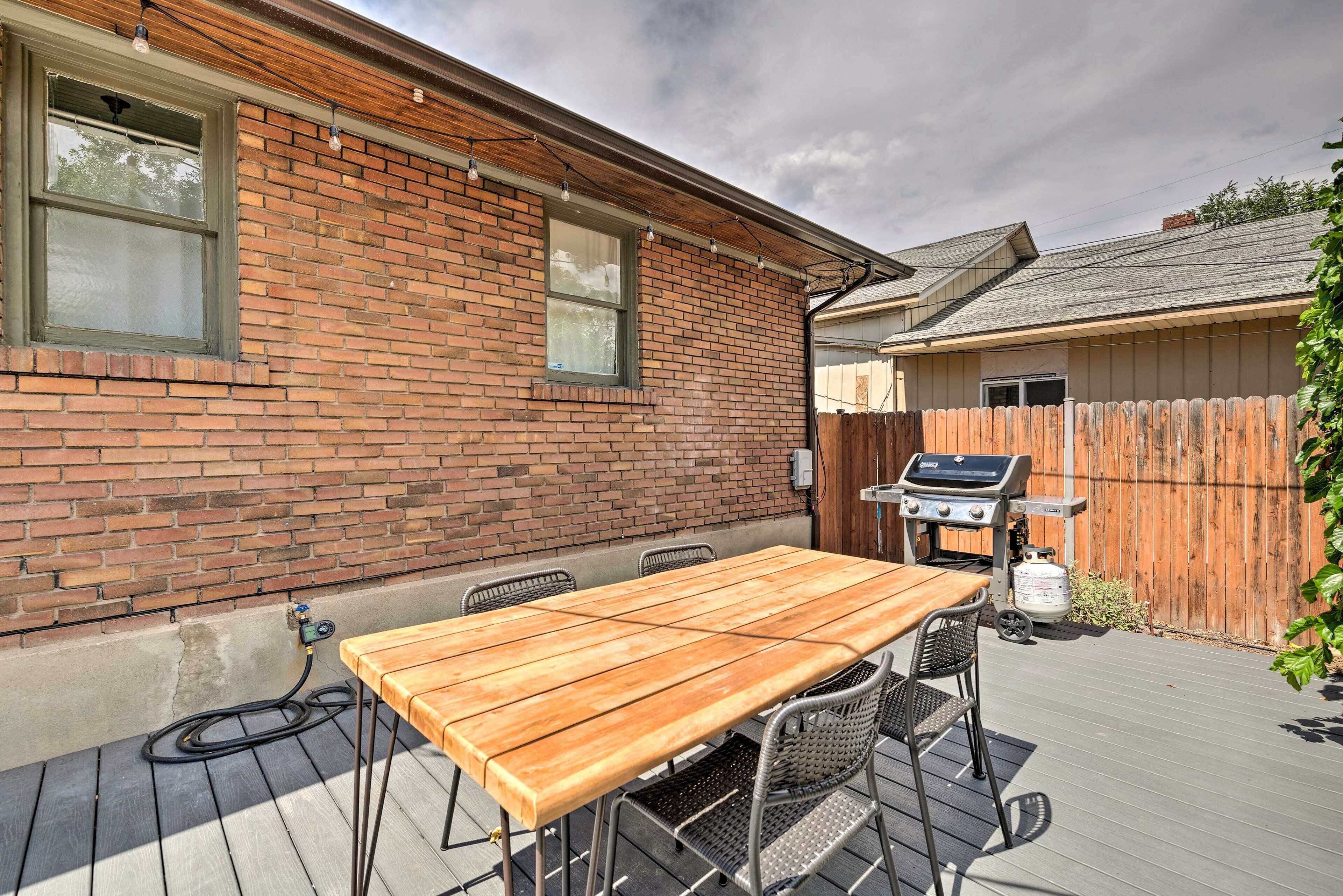 A patio with a wooden table and chairs, a barbecue grill, and a brick wall.