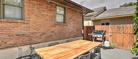 A patio with a wooden table and chairs, a barbecue grill, and a brick wall.
