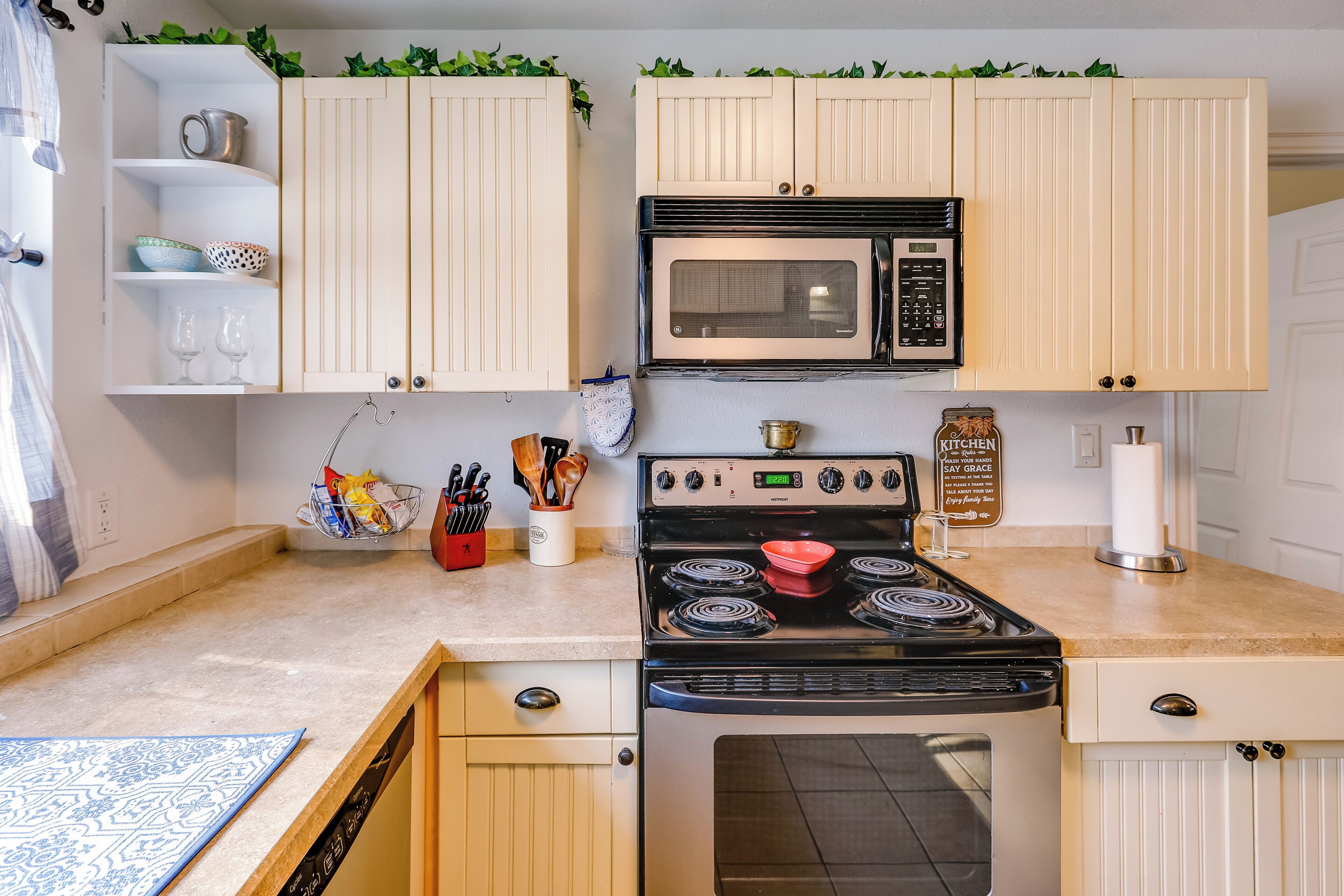 A kitchen with white cabinets, a stove, a microwave, and a sink.