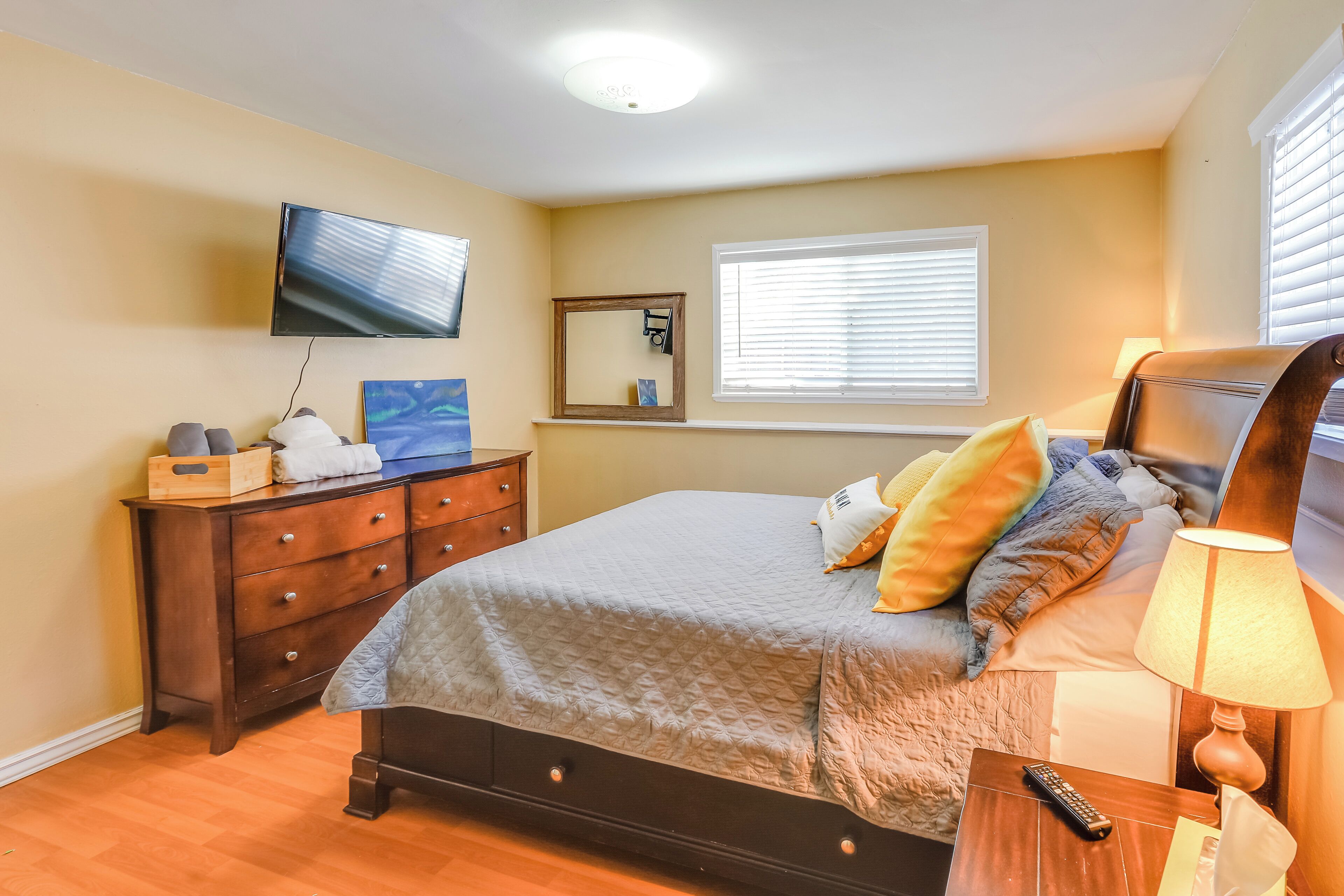 A bedroom with a bed, dresser, TV, and bedside lamp.