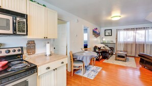 A compact kitchen with a stove, microwave, and cabinets. There is a dining area with a table and chairs, and a living room with a couch and a small table.