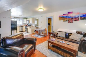 A modern living room with a leather sofa, a wooden coffee table, and a dining area with a table and chairs. A kitchen with a refrigerator and a microwave is visible in the background. - 2 Mi to Dtwn: Cozy Getaway in Fairbanks! (Fairbanks)