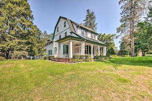 A two-story house with a green roof and white walls, surrounded by a well-maintained lawn and tall trees. - 3-acre Property: Charming Dutch Country Colonial (Sinking Spring)