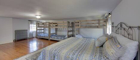 Una camera da letto con un letto grande, due letti a castello, testiere in legno, un termosifone e una finestra con tende.