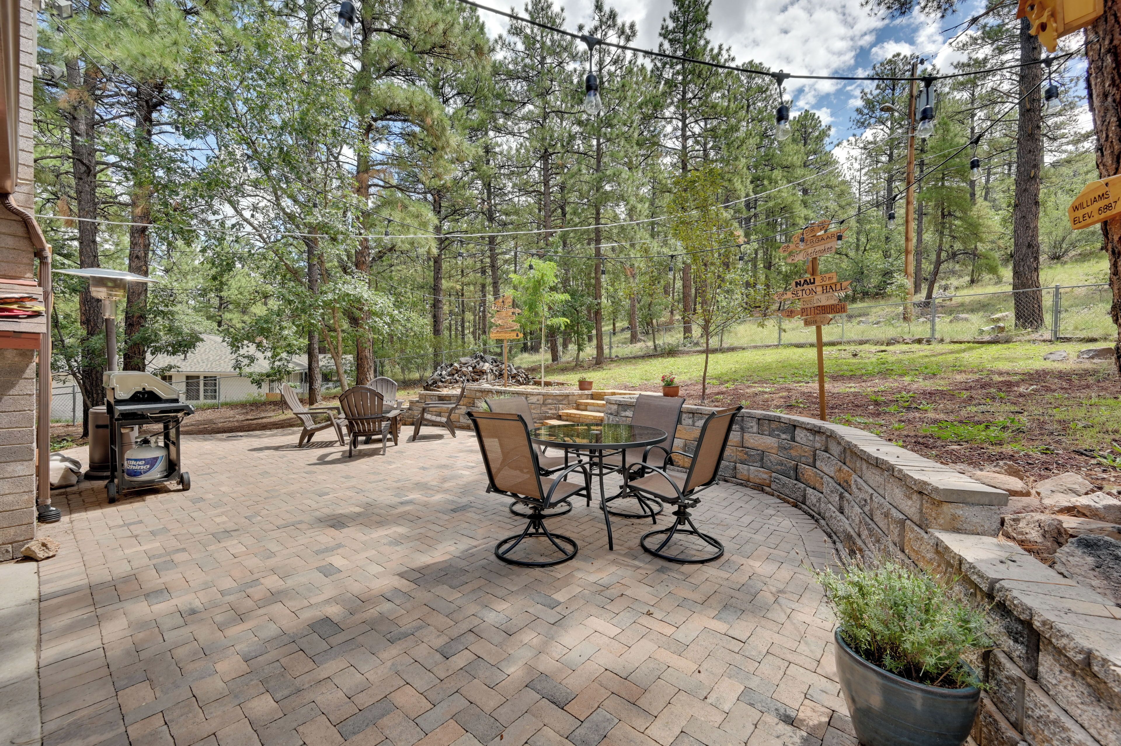 Eine Terrasse mit Pflasterboden, einem runden Tisch und vier Stühlen. Übertöpfe mit Pflanzen und eine Steinmauer sind zu sehen.