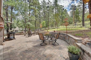 A patio with a brick floor, a round table, and four chairs. There are potted plants and a stone wall.