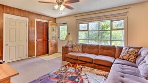 A living room with a brown leather couch, a patterned rug, a ceiling fan, and a large window with a view of trees. - Family-friendly Allentown Abode w/ Backyard! (Allentown)