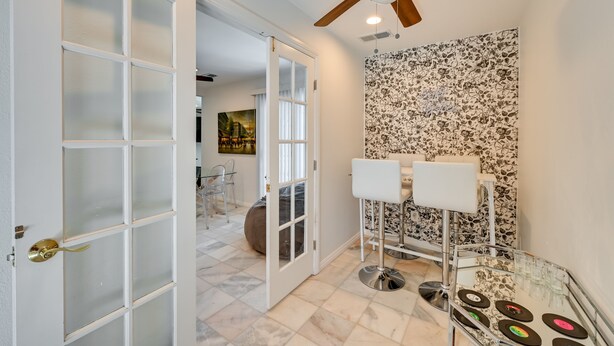 A modern room with a glass door, a ceiling fan, a bar area with stools, and a patterned wall. - El Cajon Oasis w/ Backyard 17 Mi to Dtwn San Diego (El Cajon)