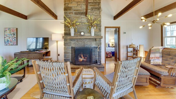 A cozy living room with a stone fireplace, wooden beams, wicker chairs, and a television. - Hike, Fish & Relax: Family Boone Gem w/ Views! (Boone)