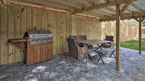 Une terrasse extérieure dotée d’une pergola en bois, d’un barbecue et de mobilier en osier.