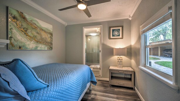 Une chambre à coucher comprenant un lit, un ventilateur de plafond, une table de chevet, une fenêtre et des œuvres d’art accrochées aux murs.