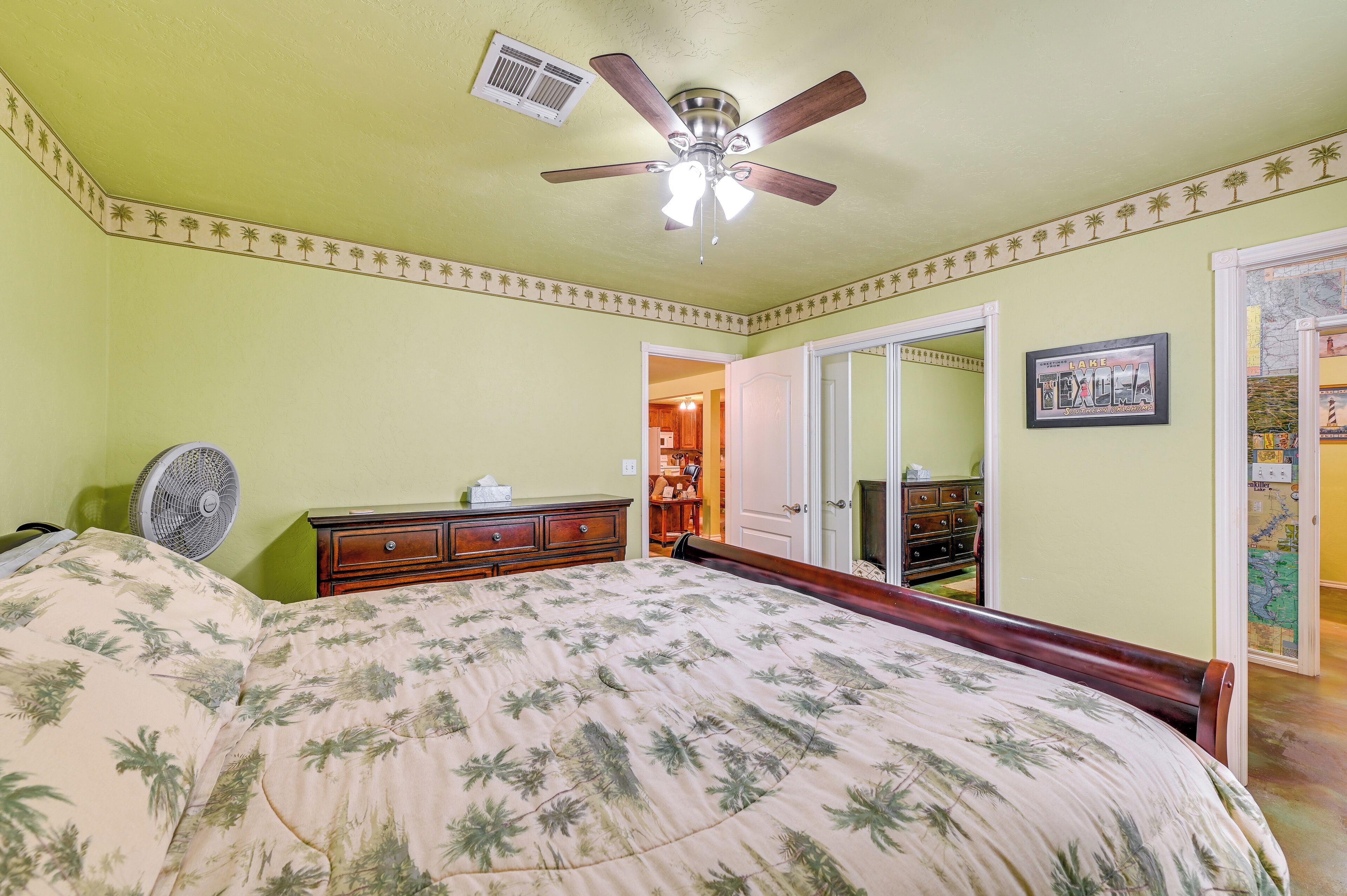 A bedroom with a bed, a ceiling fan, a dresser, and a door leading to another room.