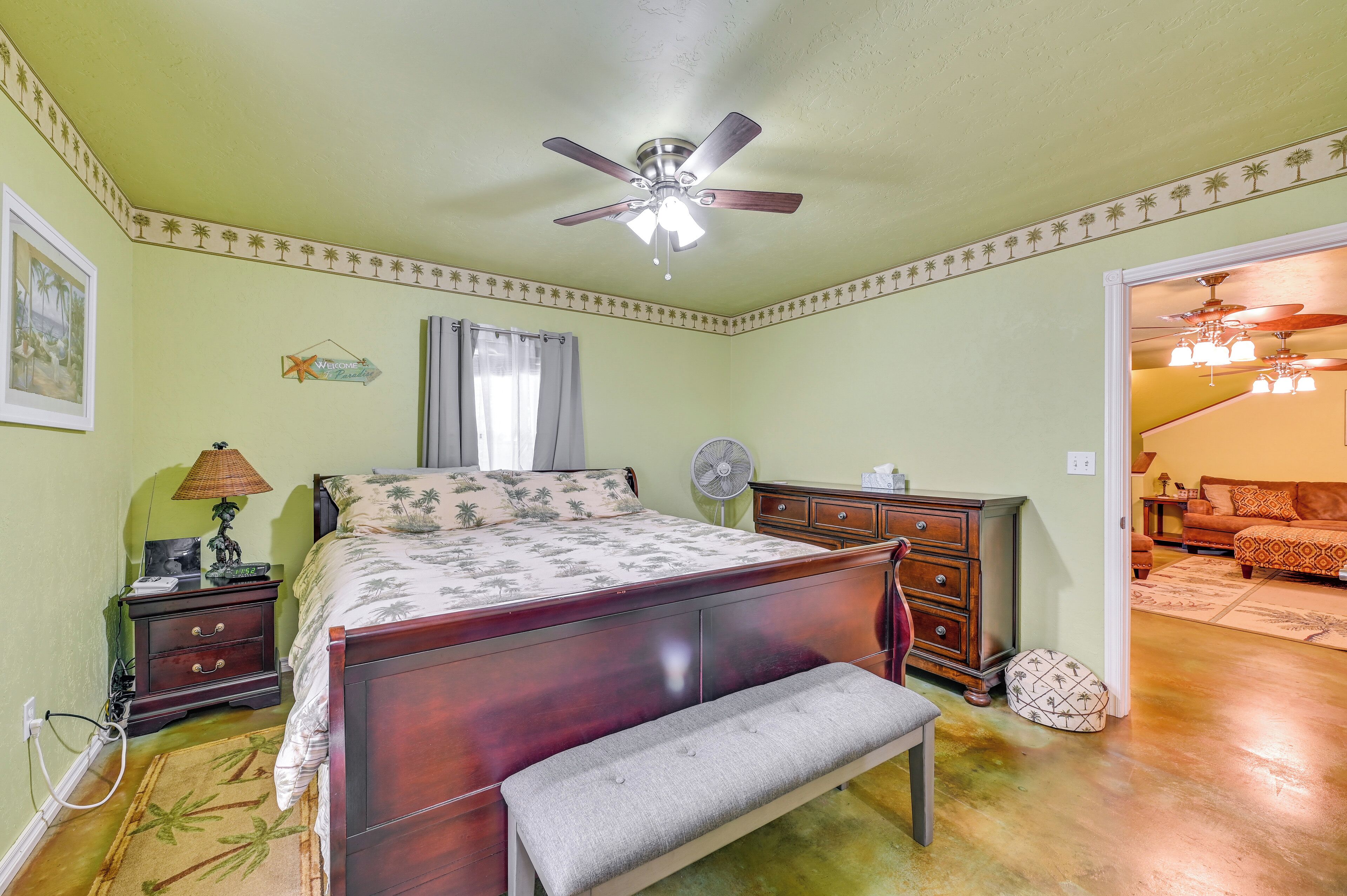 Une chambre à coucher comprenant un lit, un banc, un ventilateur de plafond, une table de chevet, une lampe et un ventilateur.