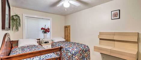 A bedroom with two beds, a ceiling fan, a wooden headboard, a small bedside table, and a window with blinds.