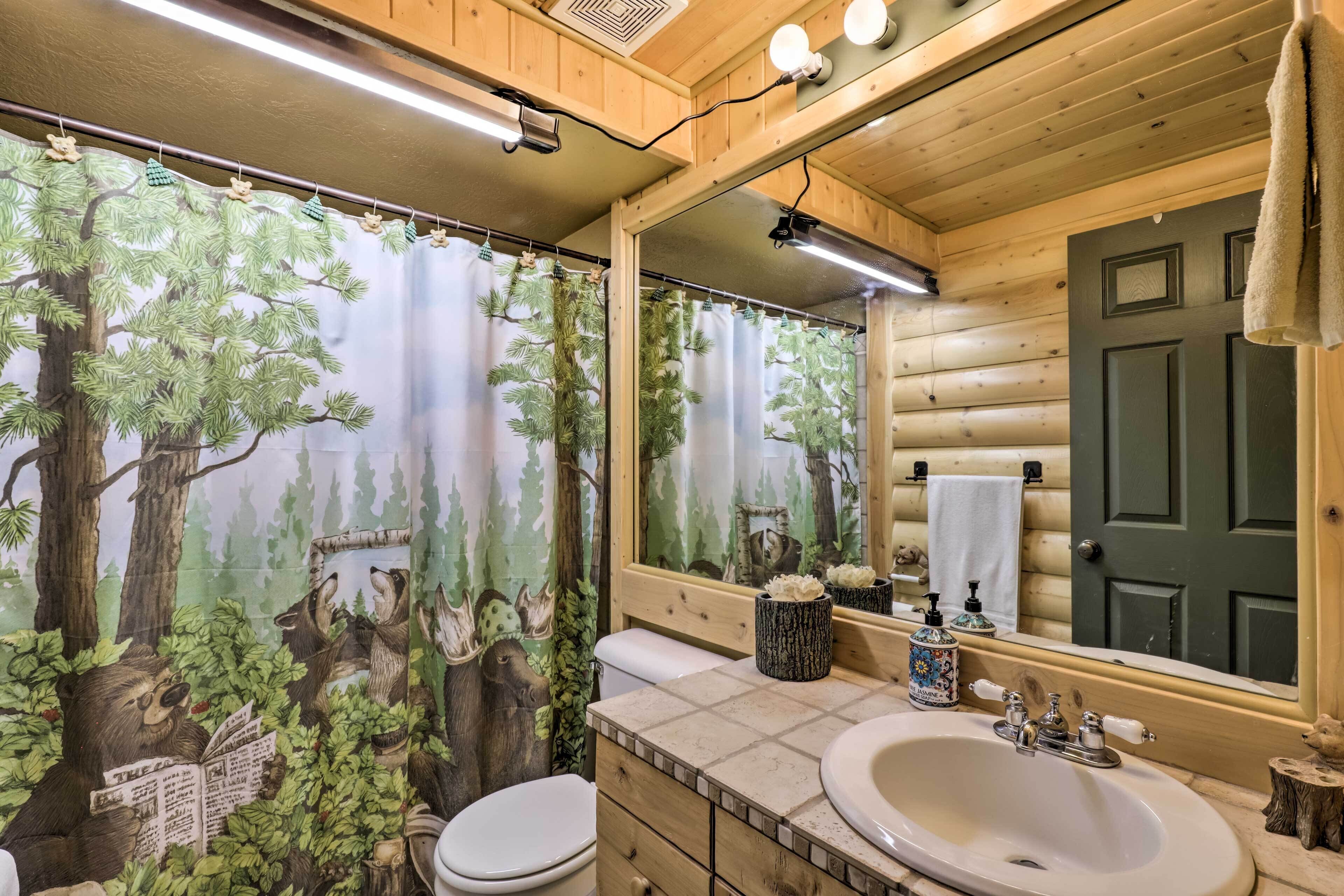 A bathroom with a forest-themed shower curtain, a wooden vanity with a sink, and a mirror above the mirror.