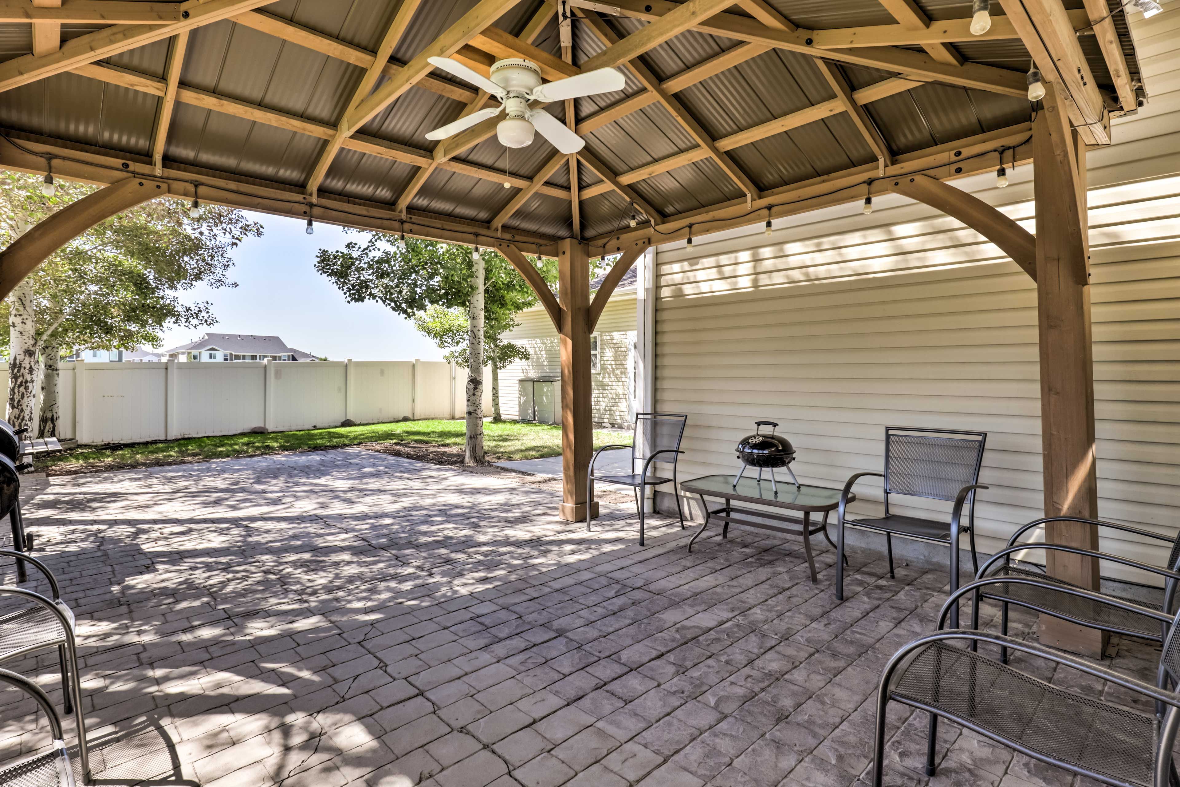 A covered patio area with a ceiling fan, metal chairs, and a grill table.