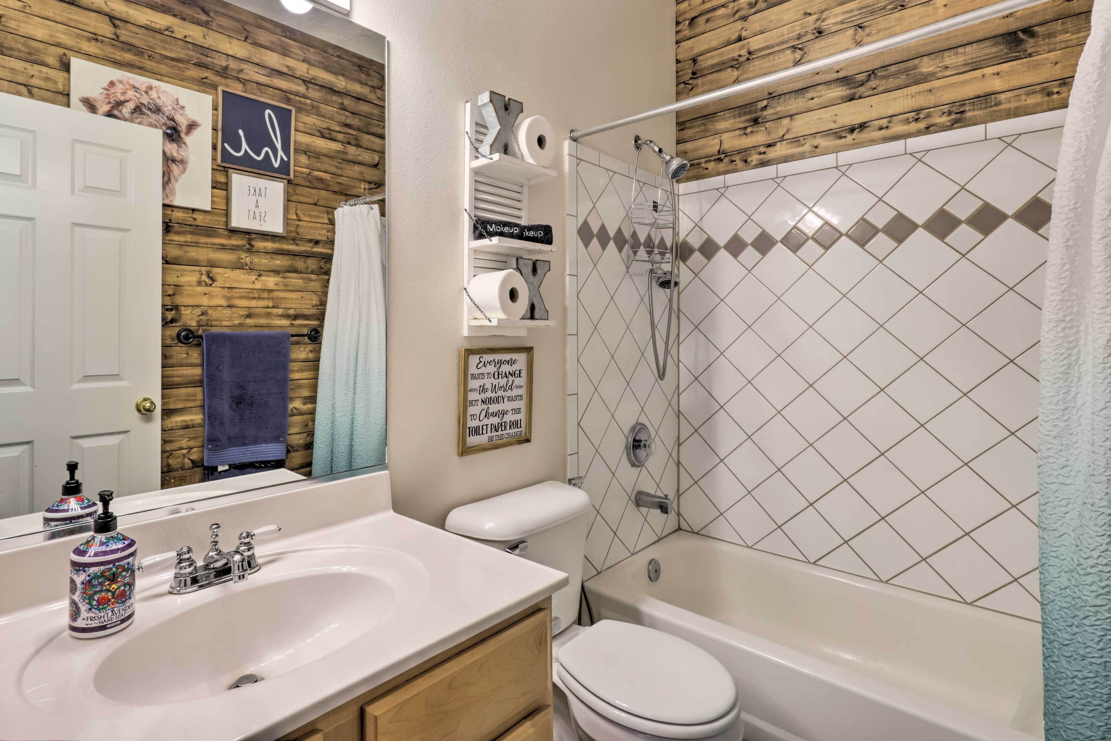 A bathroom with a wooden wall, a white sink, a toilet, and a shower.