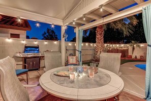An outdoor patio with a round table, chairs, a grill, and a pool.